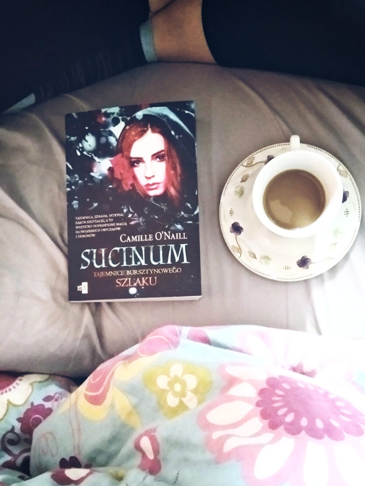 Sucinum - Recenzja książki -Książka na tle pościeli, obok niej kubek z kawą