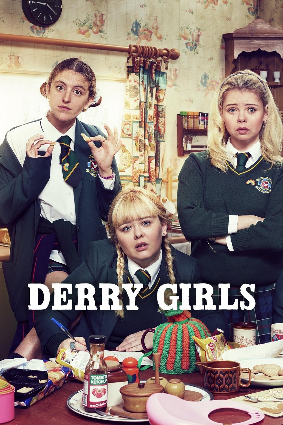 Grupa dziewczyn obok dużego stołu. Na środku tytuł - Derry Girls